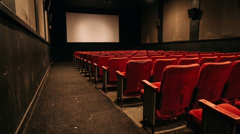 Rangée de fauteuils rouges vides dans une salle de cinéma, écran blanc éclairé au fond